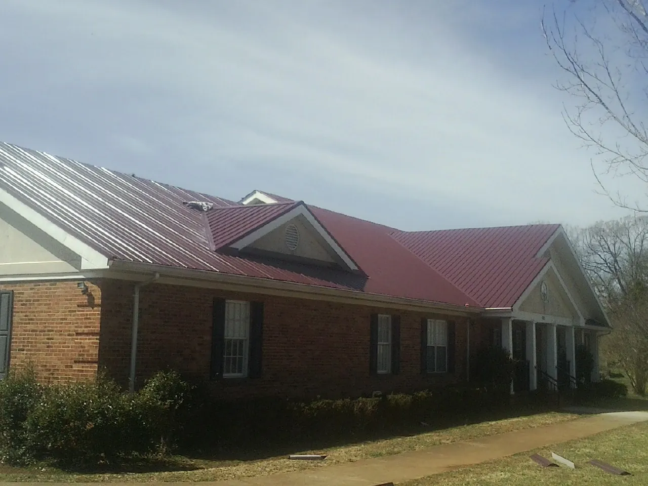 Red metal roof with gabled entries on a long brick building, from a Hail Damage Roof Repair job in Lakeside