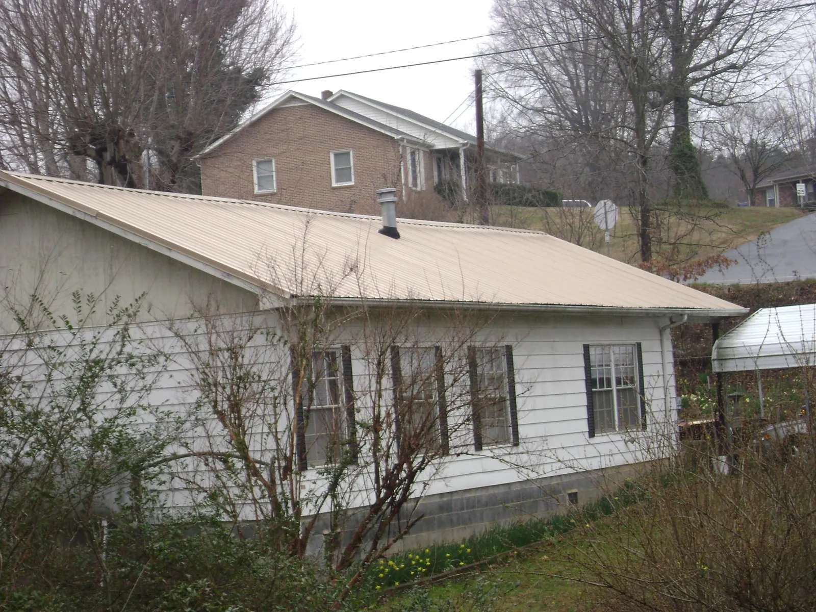 Tan metal roof on a white sided house set into a hillside — Commercial Roofing by Roofing Brothers in Lakeside